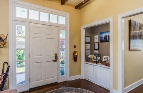 A front entryway with yellow walls, a white door and wood beams on the ceiling