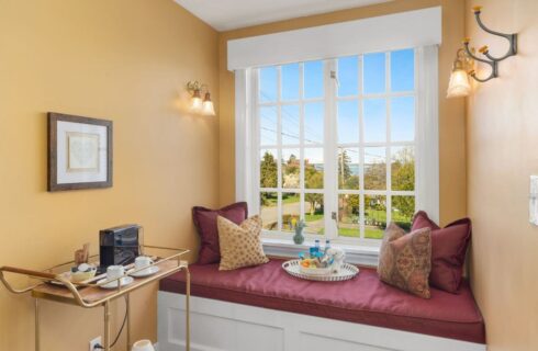 A sitting bench below windows with a tray of goodies and drinks on the bench, with views of trees and the ocean, along with a cart with a coffee center ready for guests.