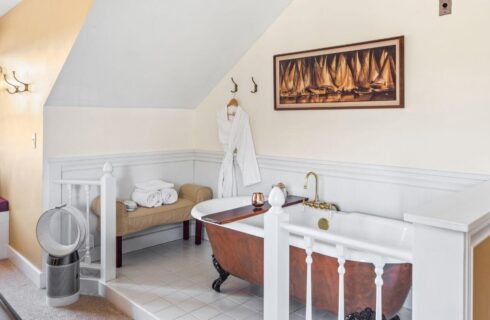 A bathtub area in a bedroom with a clawfoot tub, a bench with towels, and a bathrobe hanging from a hook