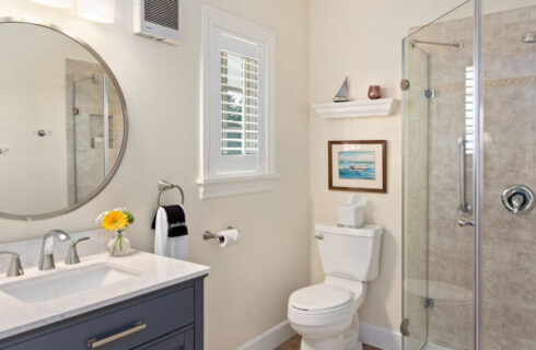 A stylish bathroom with a single sink in a vanity, a round mirror above it, a toilet, and a shower with clear shower doors