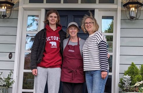 Two smiling women and a man in front of the doorway of a house.