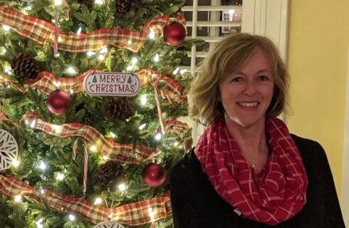 A smiling woman next to a lit Christmas tree.