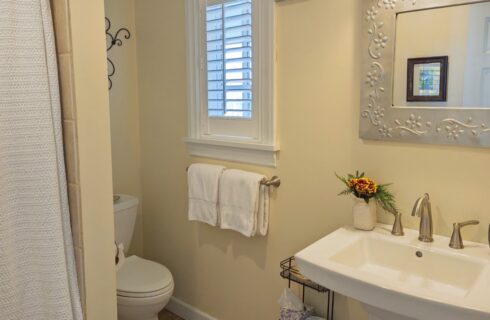 A bathroom with yellow walls, white trim, a single sink with a bouquet of flowers, and a mirror above the sink