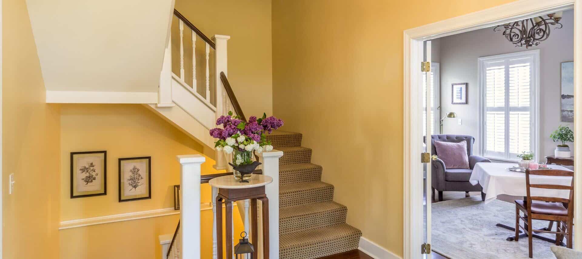 A foyer with yellow walls, white trim, open doors leading to a dining area, and stairs leading to a second floor.