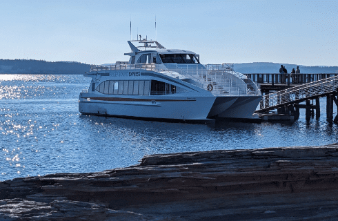 A large whale watching boat on blue glistening waters with mountains in distant the background