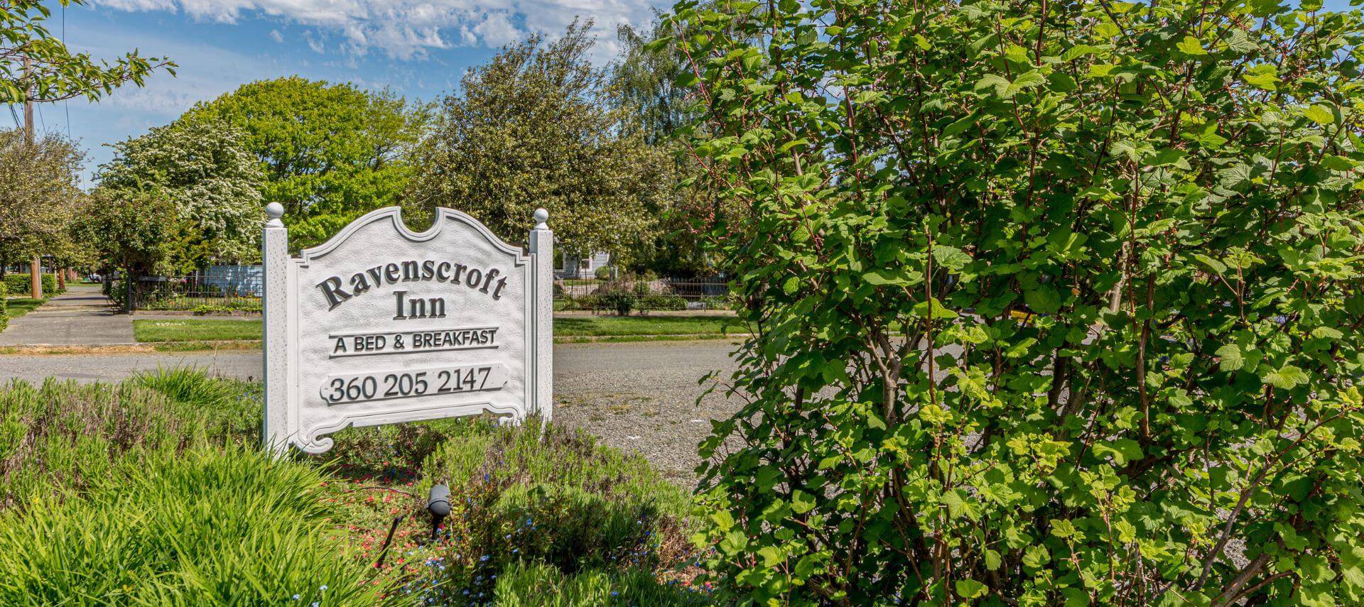 A street lined with grass, sidewalks and bushes, and a white sign that says Ravenscroft Inn A Bed & Breakfast and a phone number 306-205-2147